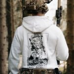 white hoodie from The Trace depicting Light Infantry design with a soldier standing with a heavy backpack