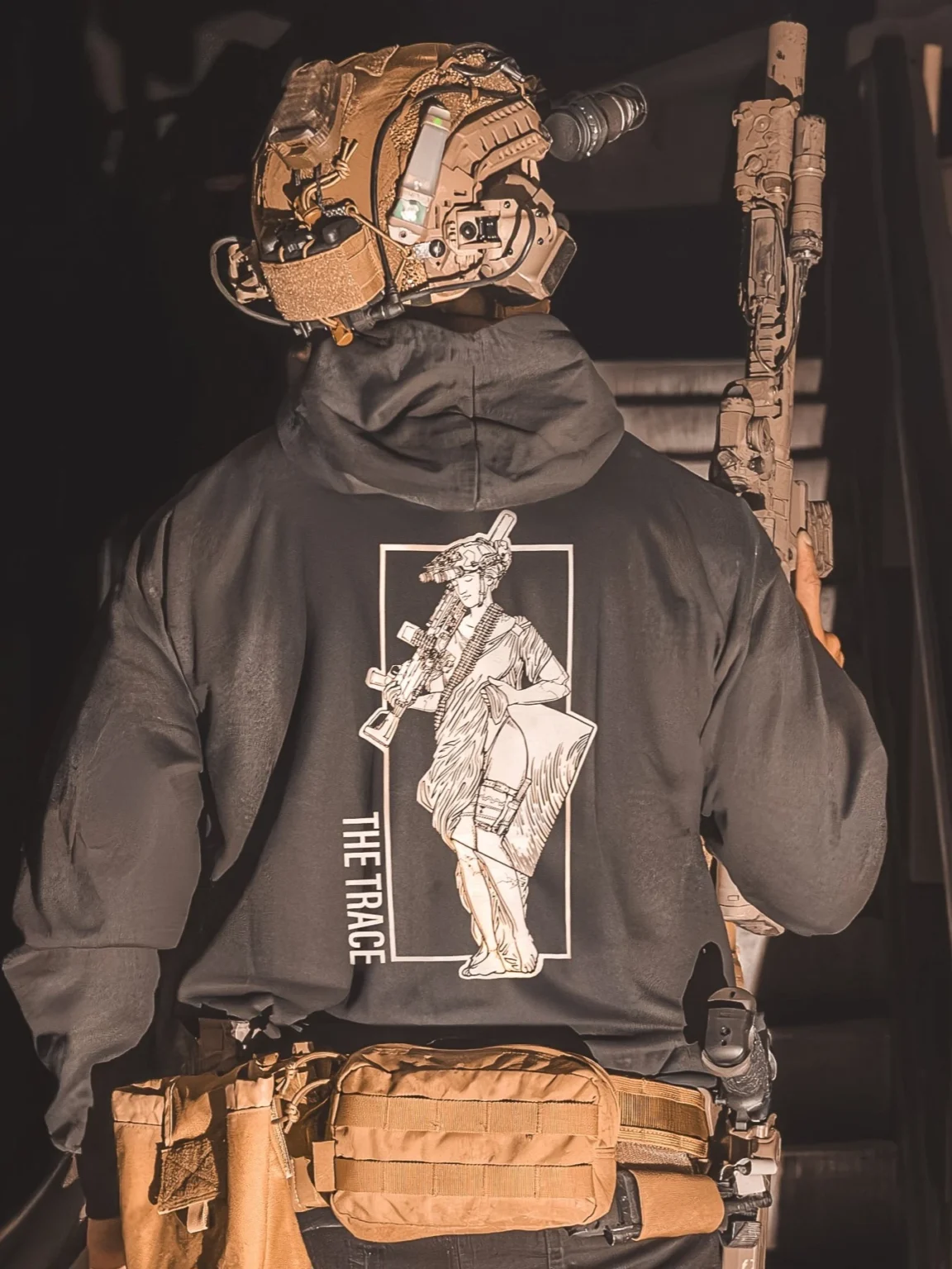 Hoodie noir de The Trace avec une fille portant une mitrailleuse