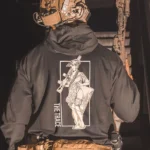 black hoodie from The Trace featuring a girl carrying a machinegun