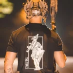black shirt from The Trace featuring a girl carrying a machinegun