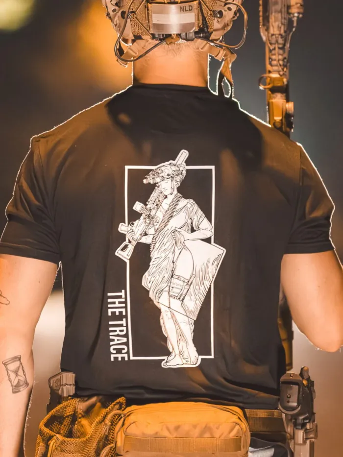 black shirt from The Trace featuring a girl carrying a machinegun