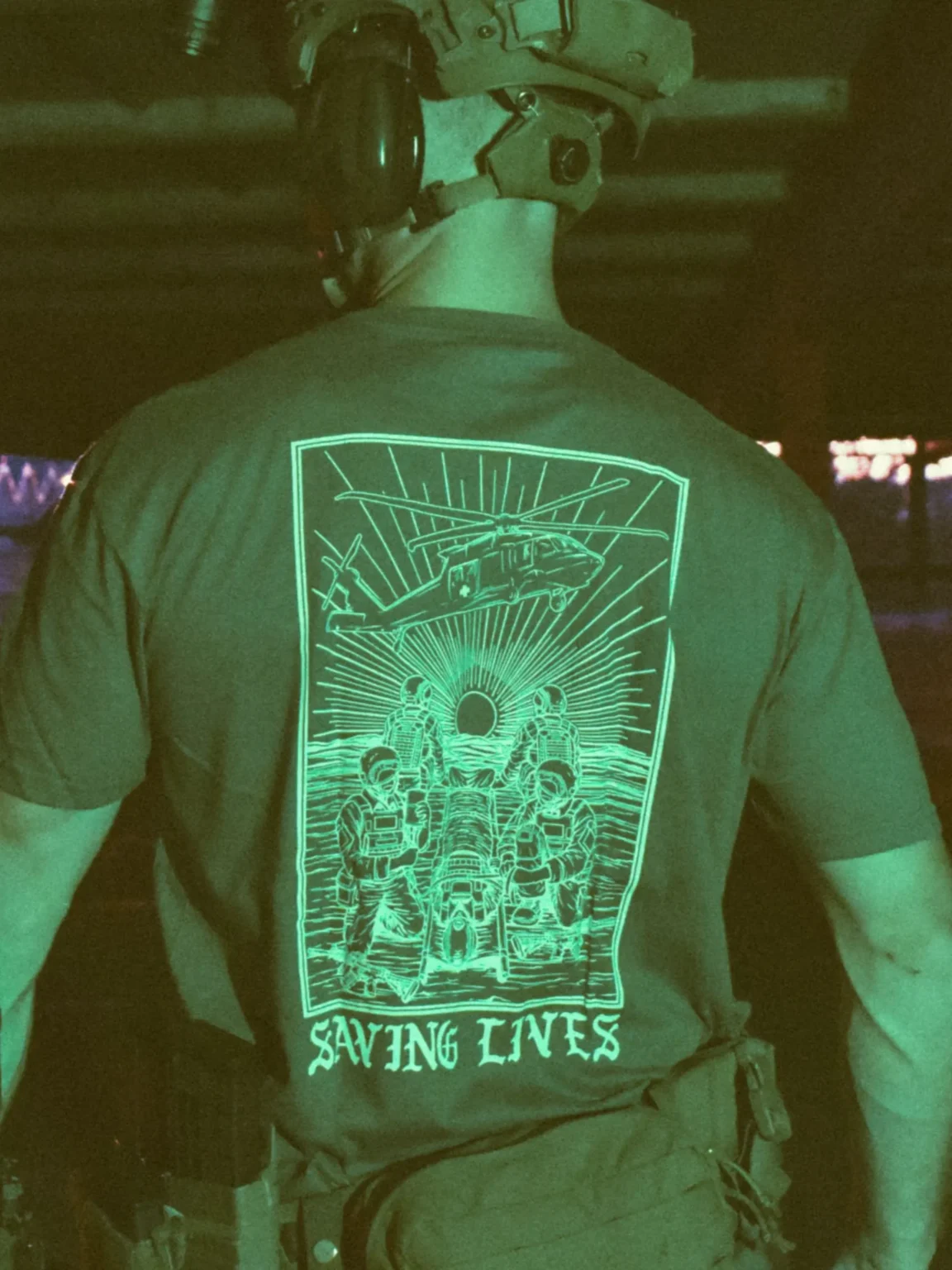 Saving-lives-charcoal-shirt-edit Cotton T-shirt with Saving Lives artwork showing soldiers in action, holding a stretcher during a tense medevac moment with a helicopter descending nearby.