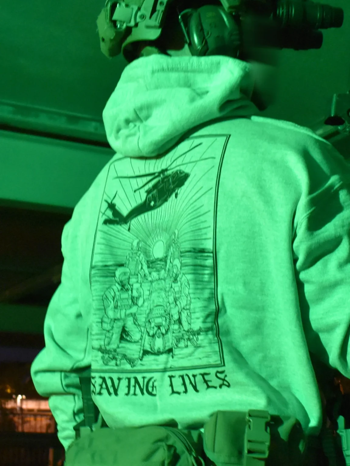 Saving-lives-heather-grey-hoodie-edit Military-style hoodie featuring the Saving Lives design: a group of soldiers carrying a stretcher while a helicopter prepares to land, symbolizing courage under pressure.