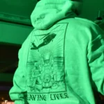 Military-style hoodie featuring the Saving Lives design: a group of soldiers carrying a stretcher while a helicopter prepares to land, symbolizing courage under pressure.