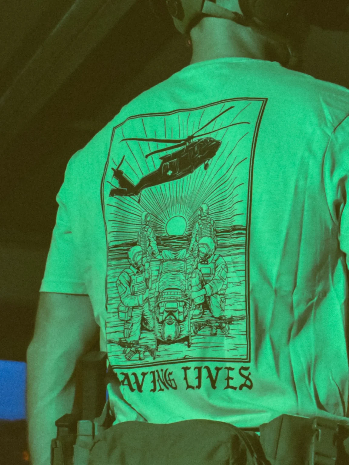 Saving-lives-sand-shirt-edit Cotton T-shirt with Saving Lives artwork showing soldiers in action, holding a stretcher during a tense medevac moment with a helicopter descending nearby.