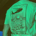 Cotton T-shirt with Saving Lives artwork showing soldiers in action, holding a stretcher during a tense medevac moment with a helicopter descending nearby.