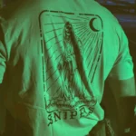 Tactical T-shirt with a skeletal sniper design, positioned on a pile of skulls and holding a high-caliber Arctic Warfare Super Magnum rifle.