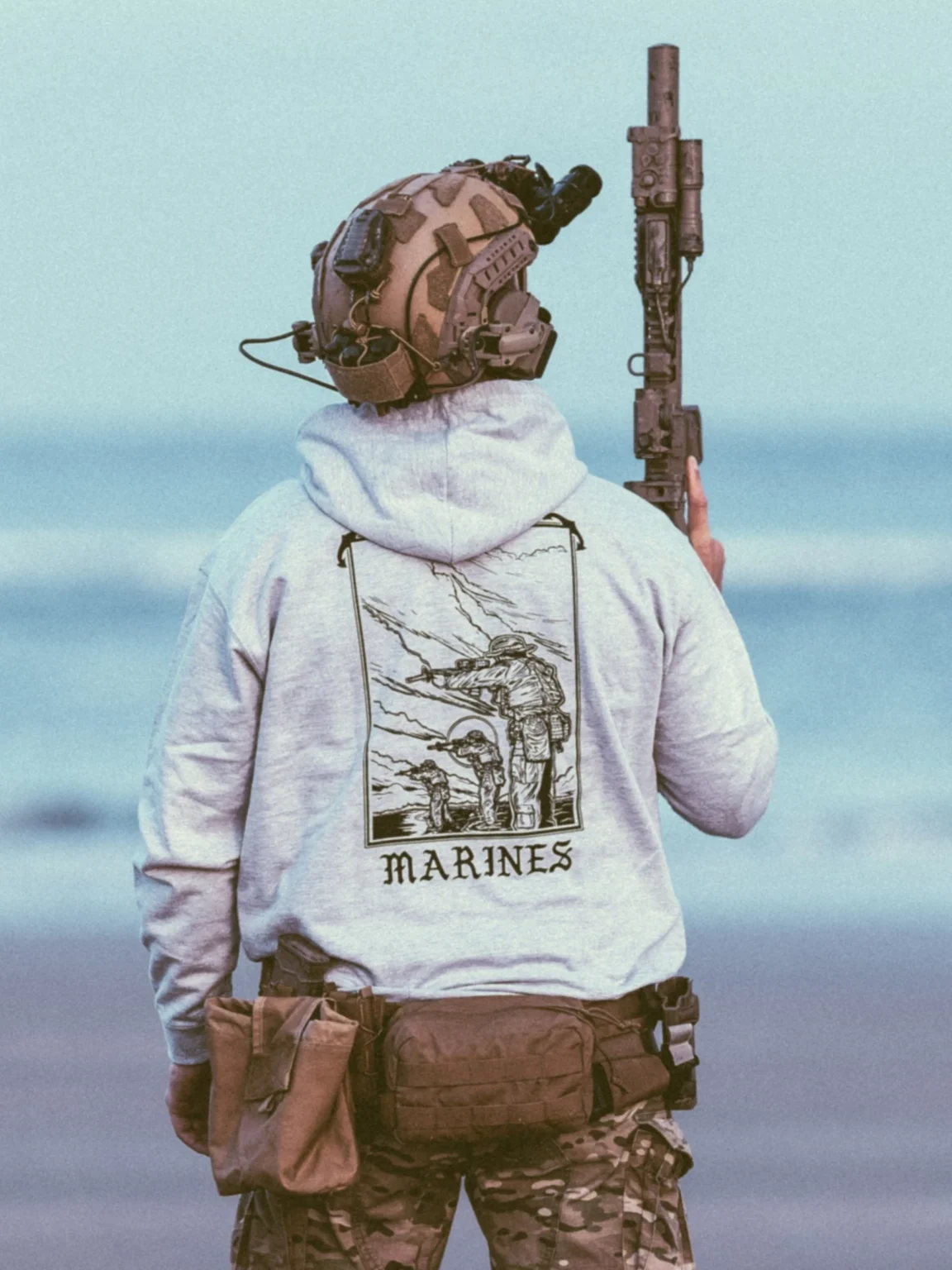 marines-hoodie-heather-grey collezione di abbigliamento The Trace con dei marines in piedi, in parte immersi nell'acqua