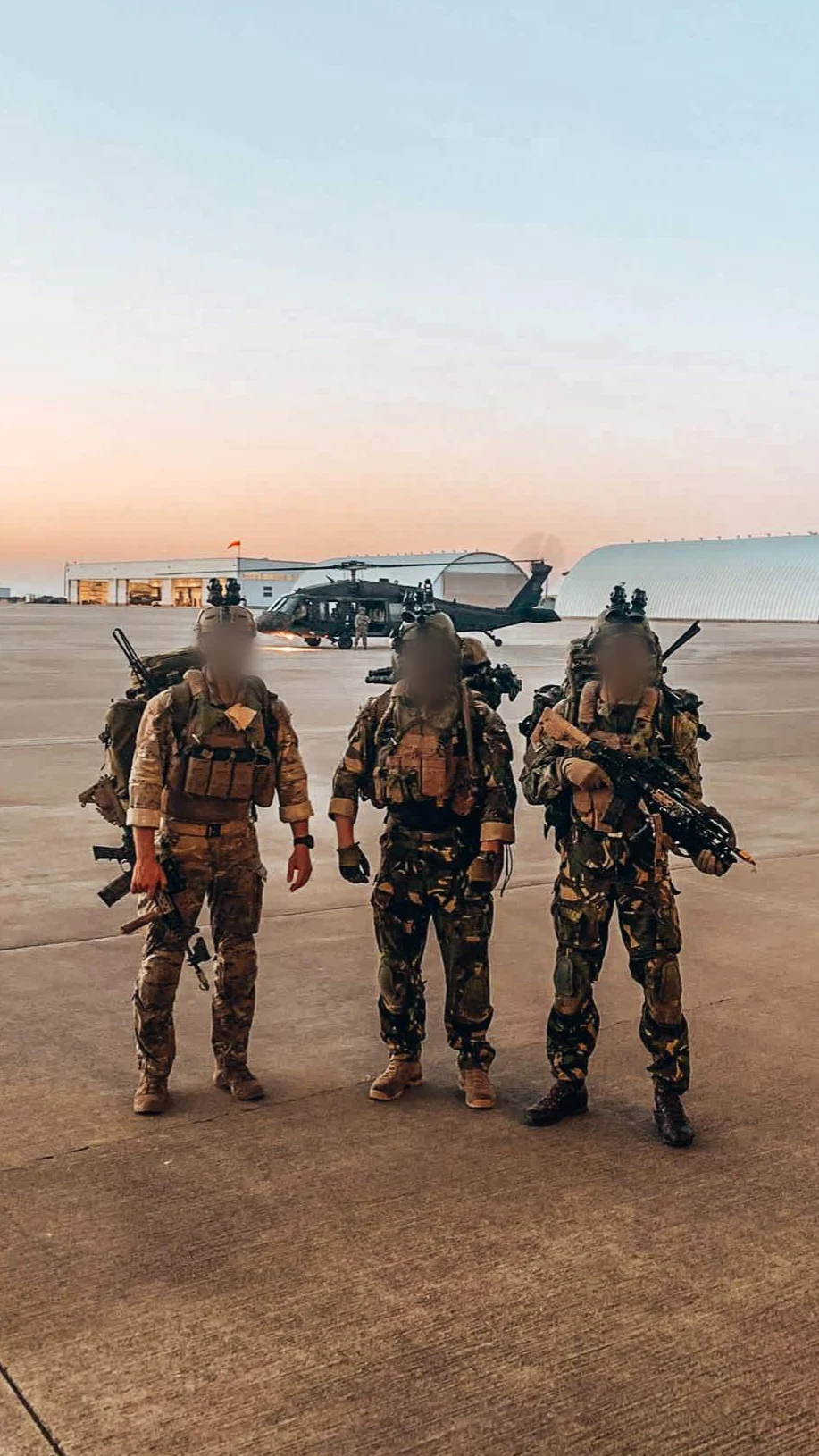 Three Dutch operators in full kit with night vision walking from a Black Hawk helicopter at dusk