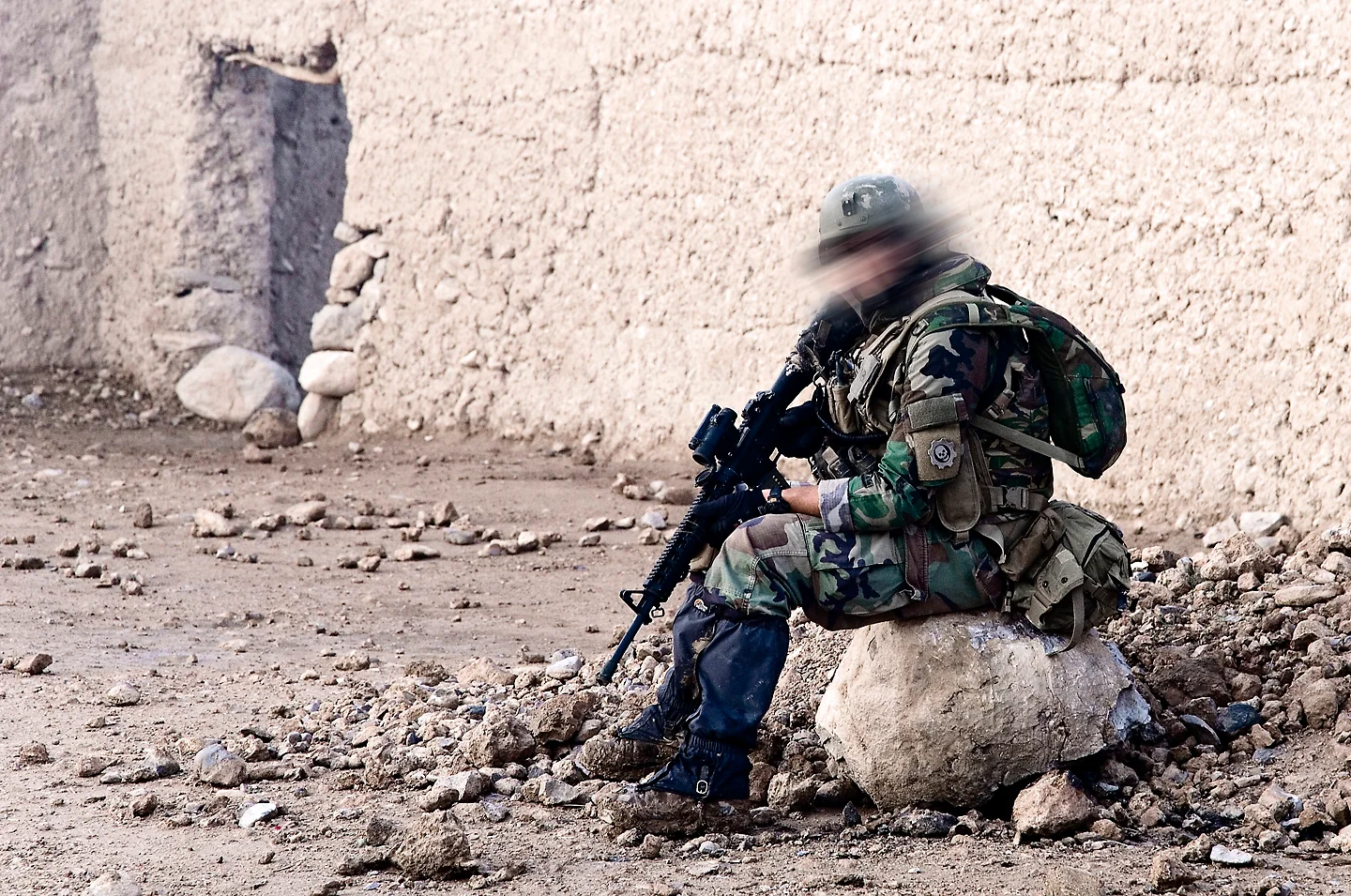 Dutch marine in woodland camouflage holding position against a mud wall, rifle up