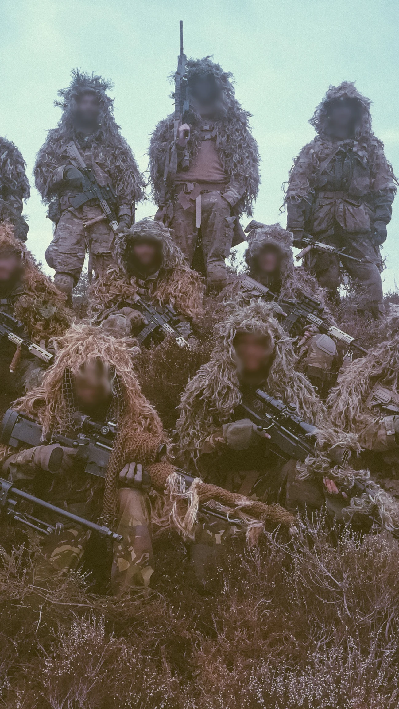 Sniper course class in ghillie suits posed together with their rifles at the end of the course