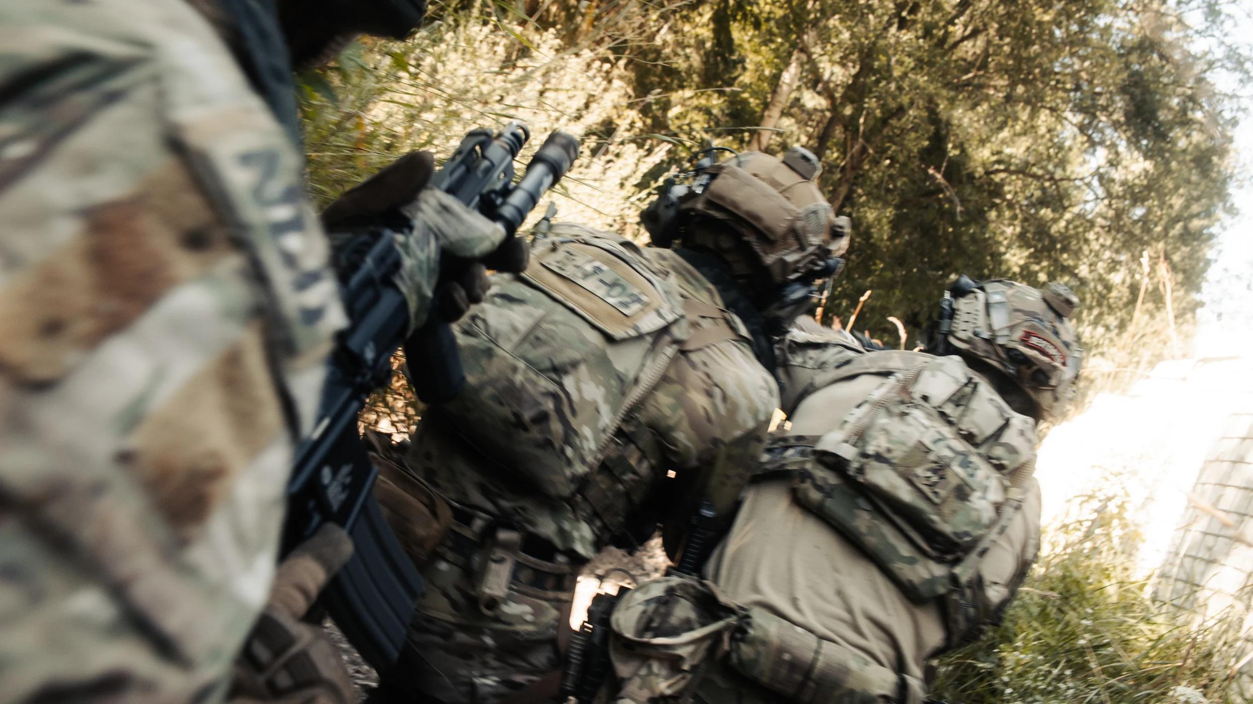 Team of soldiers in multicam moving through dense vegetation on patrol