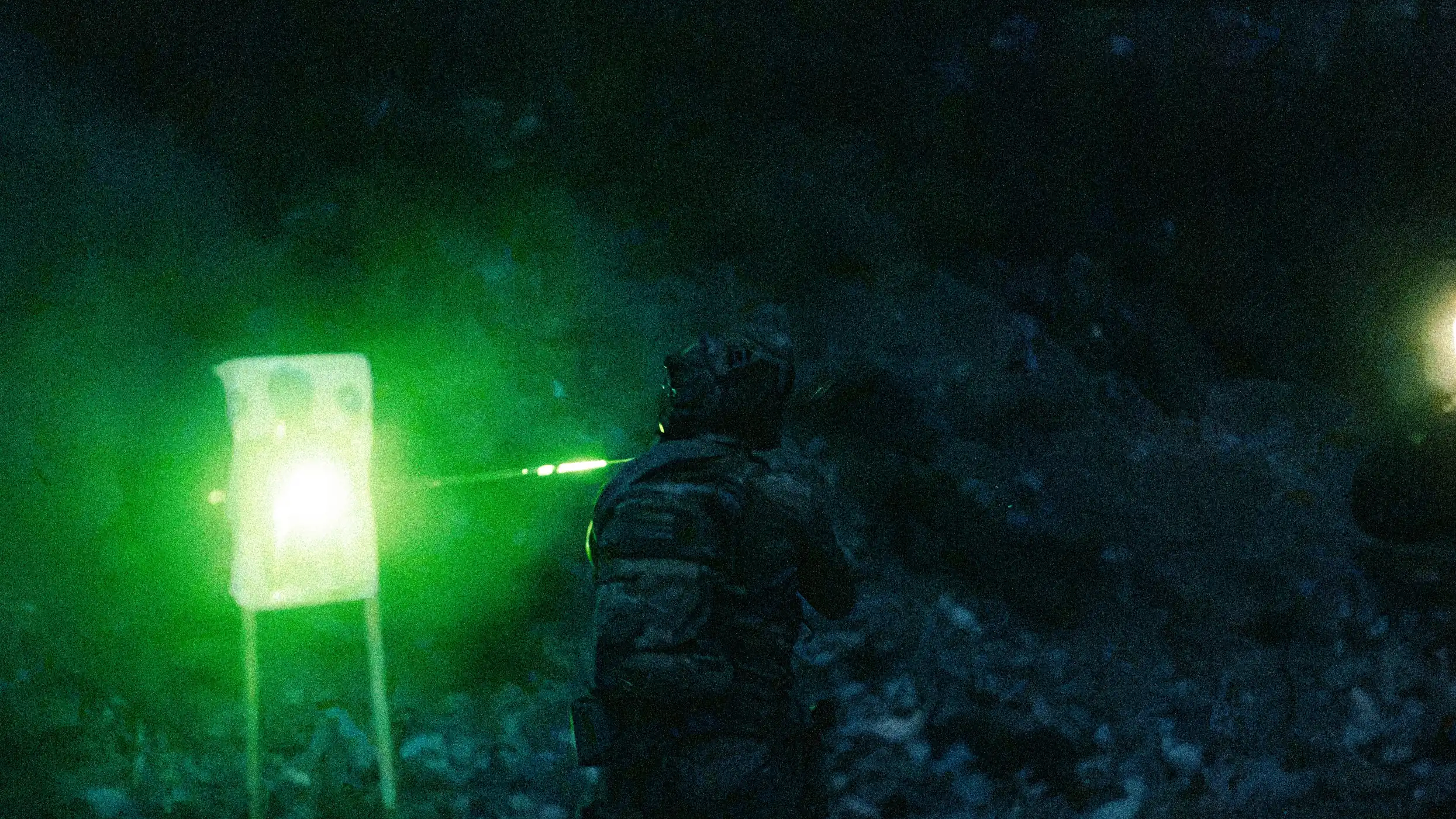 Shooter engaging a target on a night range lit by green light