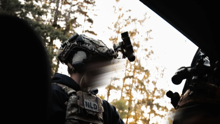 Operator with helmet, night vision mount and NLD patch moving along a treeline