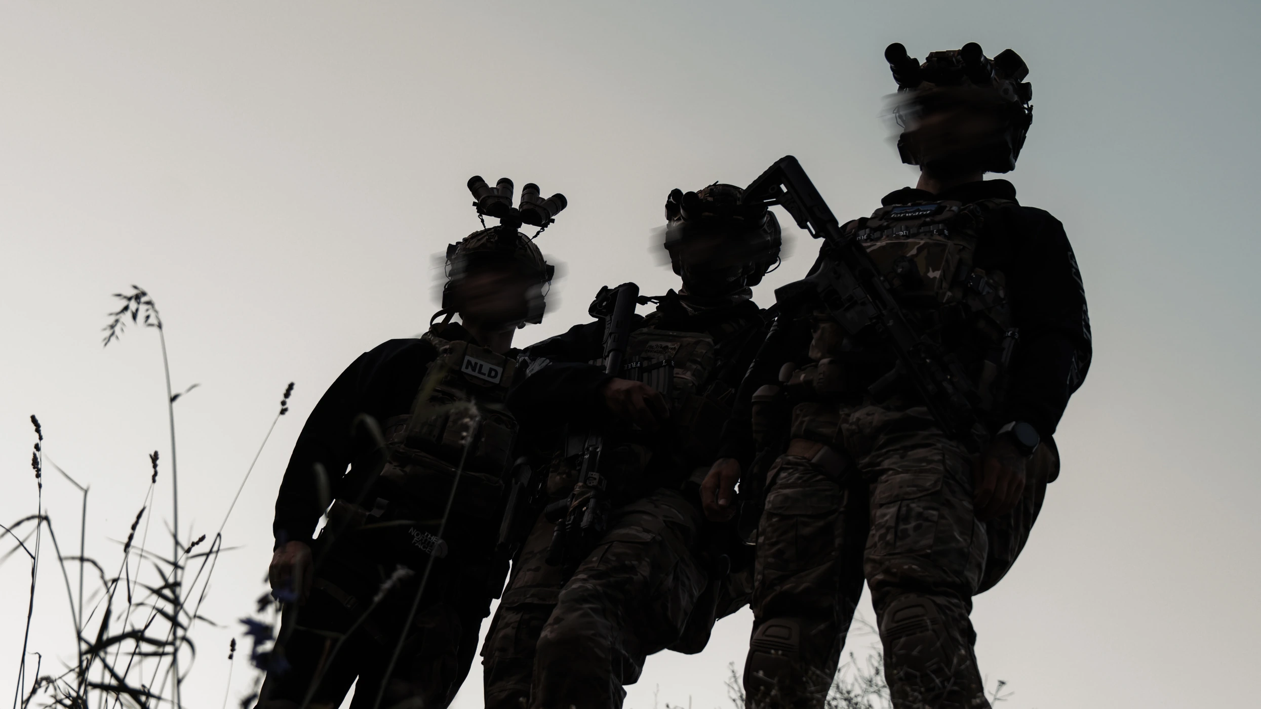 Three operators wearing The Trace apparel, silhouetted against the dusk sky with night vision mounted on their helmets