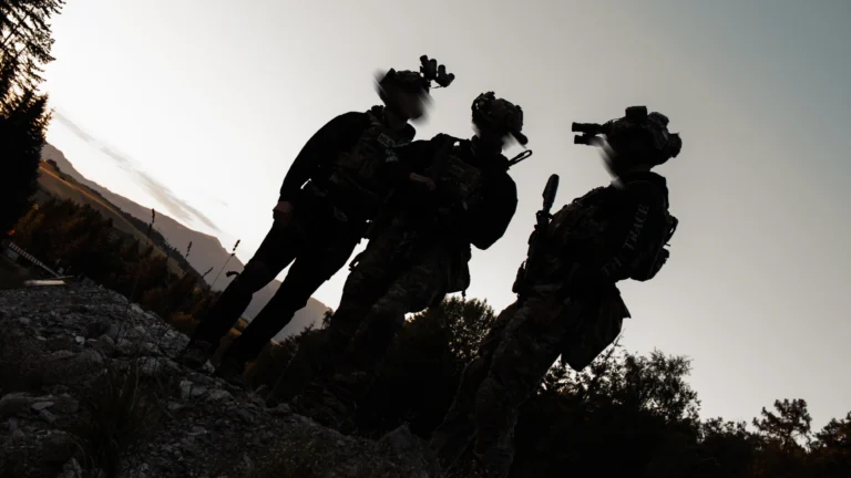 Three operators silhouetted against a bright sky on a ridge, night vision on their helmets
